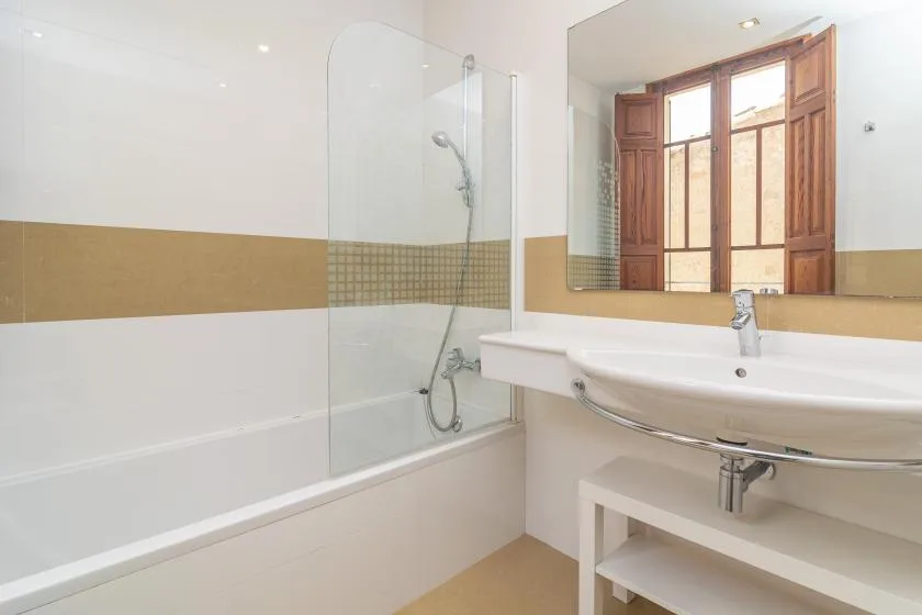Un baño luminoso con bañera, ducha y lavabo bajo una ventana con marco de madera.