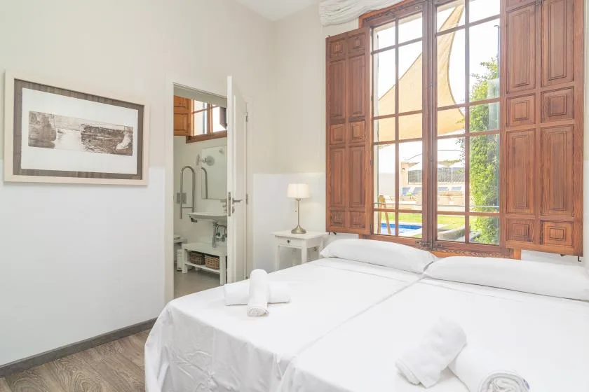 Un dormitorio luminoso con una cama tendida junto a altas ventanas con marcos de madera.