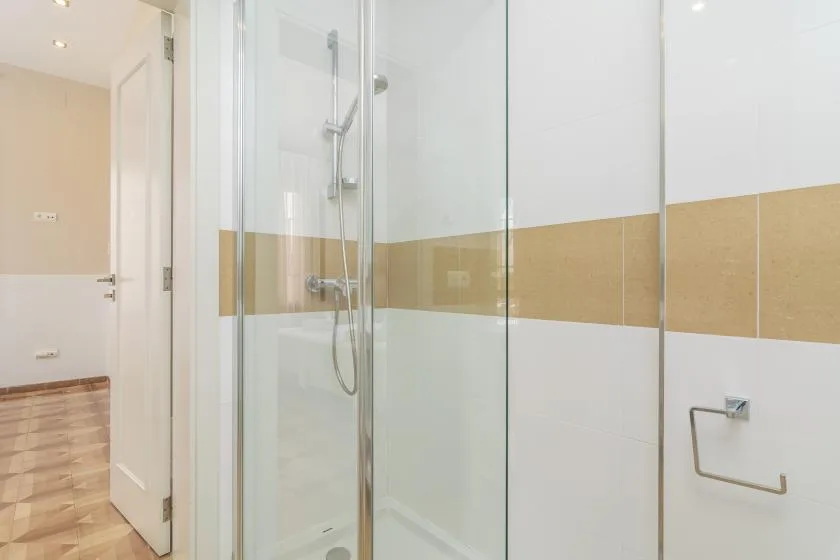 Un baño de azulejos con ducha de vidrio y una puerta hacia el pasillo.
