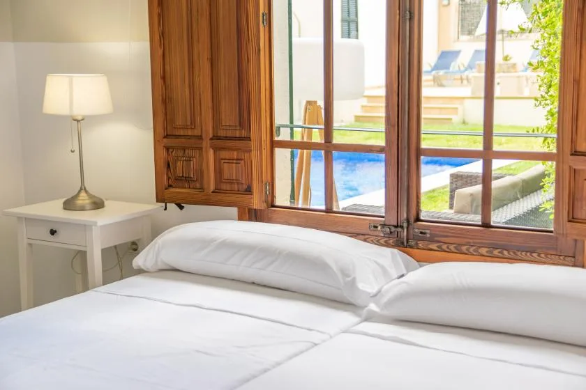 Un dormitorio con una cama blanca junto a una amplia ventana con marco de madera.