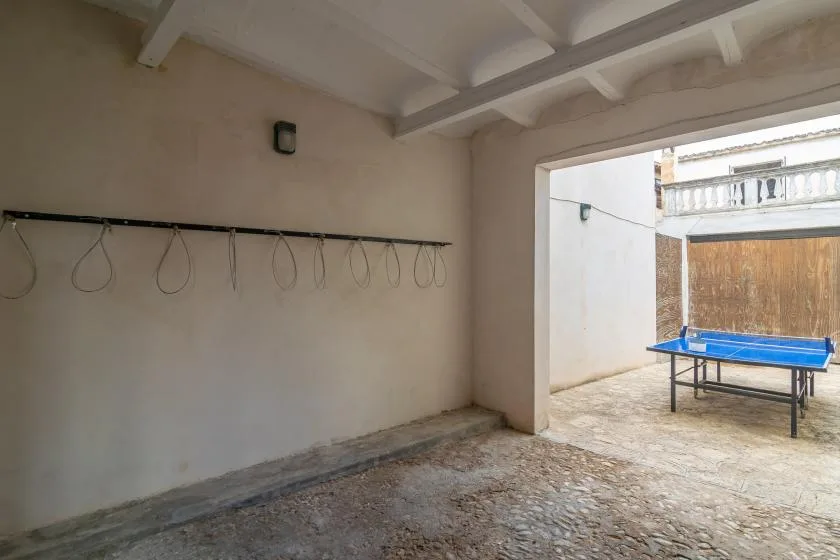 Un espacio exterior cubierto da a un patio pavimentado con una mesa azul.