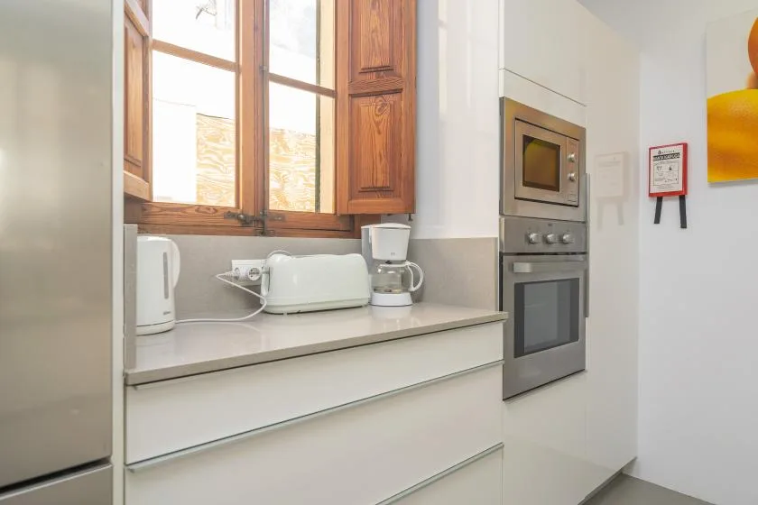 Una encimera de cocina luminosa queda bajo armarios de madera y una ventana.