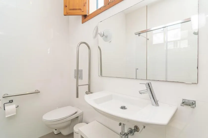 Un baño luminoso con lavabo, inodoro y un espejo grande en la pared.