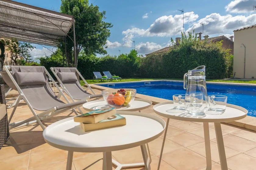 Un patio junto a la piscina con asientos y mesas al lado del agua.