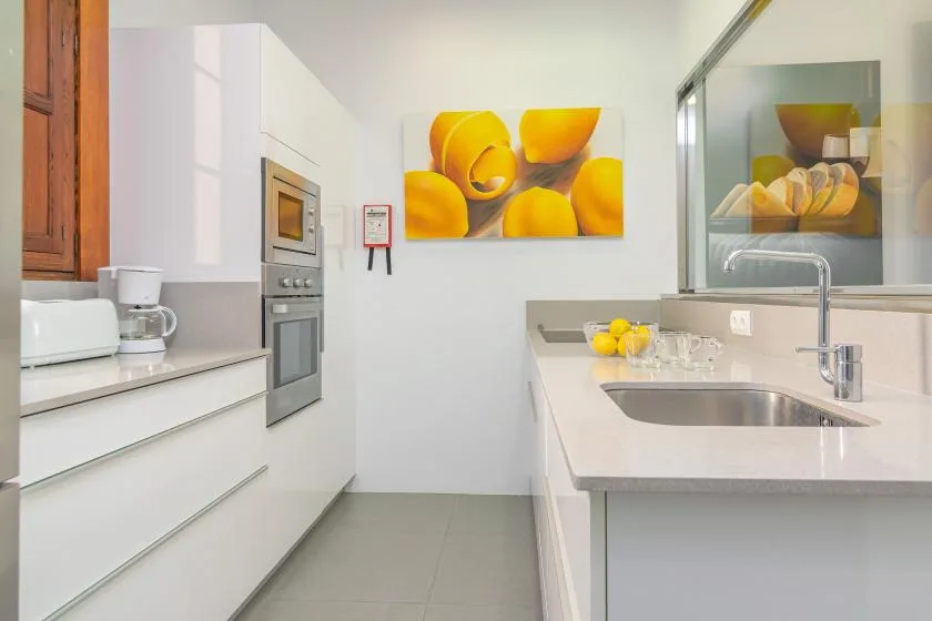 Una cocina moderna y luminosa con armarios blancos, horno integrado y fregadero.