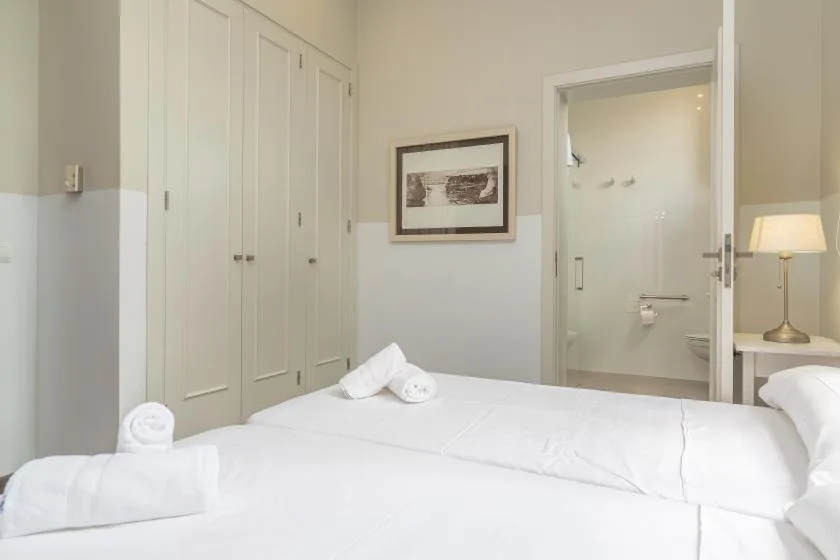 Un dormitorio luminoso con una cama bien arreglada y la puerta del baño abierta.