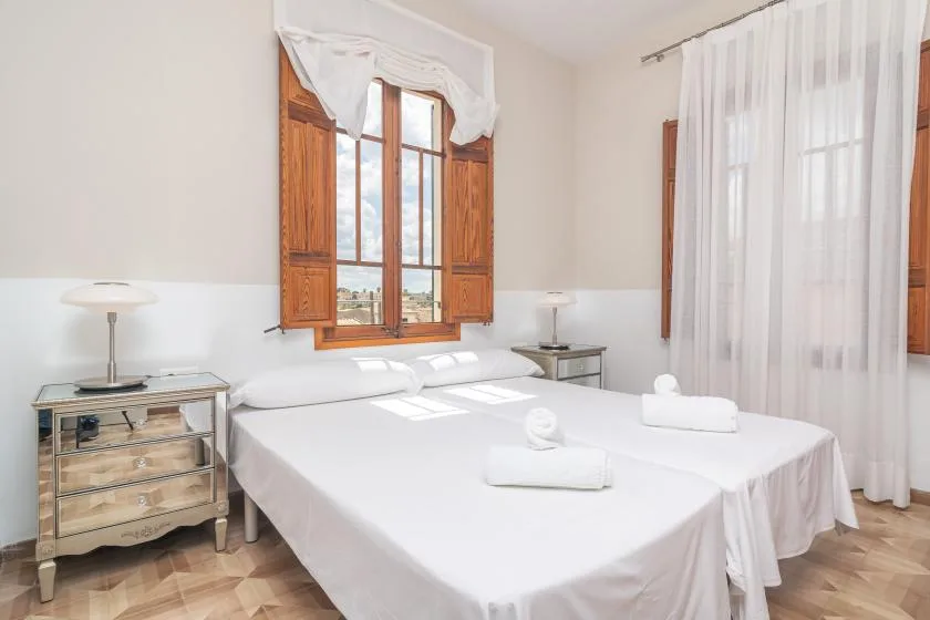 Un dormitorio luminoso con dos camas bajo una ventana con marco de madera.