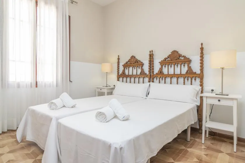 Un dormitorio luminoso con dos camas blancas y un cabecero de madera ornamentado.