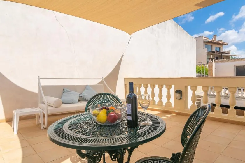 Una terraza soleada tiene una mesa redonda, asientos y una barandilla.