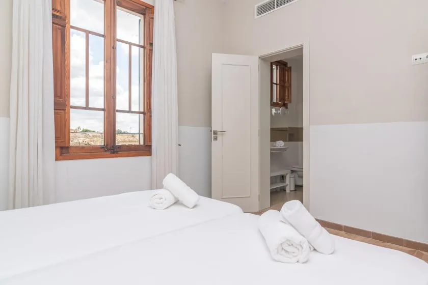 Un dormitorio con ropa de cama blanca y una ventana con marco de madera.
