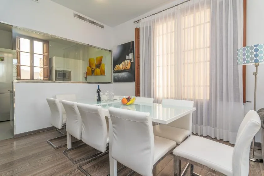 Un comedor luminoso con una mesa blanca y sillas junto a altas ventanas con cortinas.