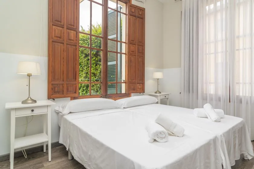 Un dormitorio luminoso con una cama grande junto a una ventana alta con marco de madera.