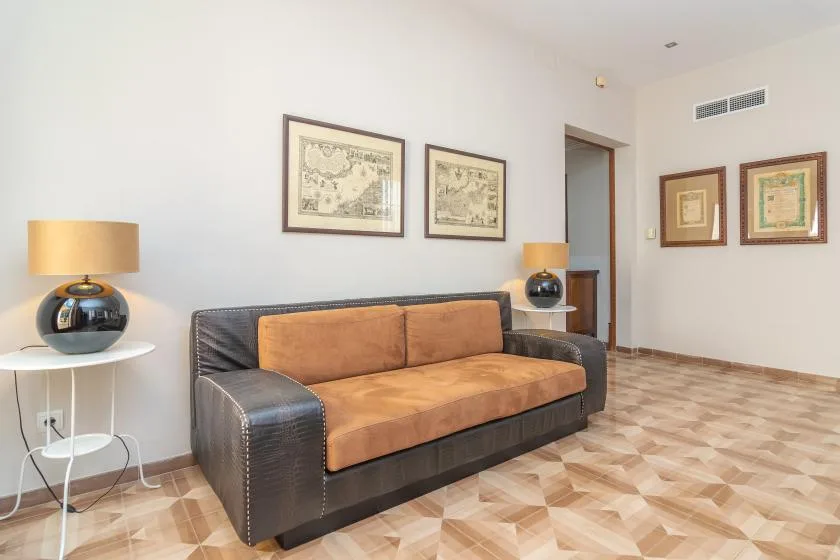 Una sala de estar con un sofá oscuro, cojines color canela y cuadros en las paredes.