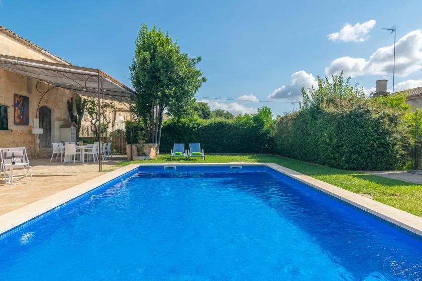 Una piscina al aire libre junto a un patio con asientos y vegetación alrededor.