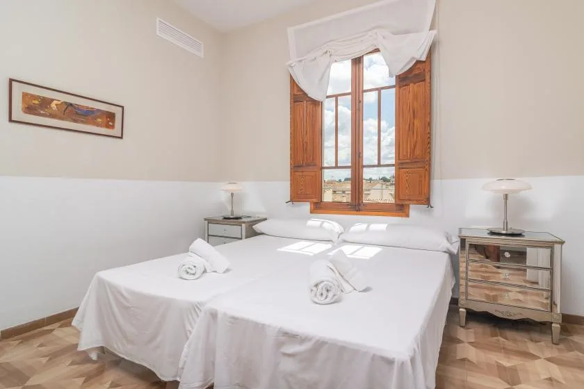 Un dormitorio luminoso con ropa de cama blanca y una gran ventana con marco de madera.