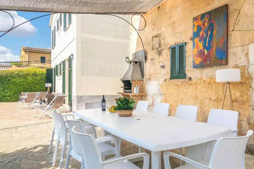 Comedor al aire libre con una mesa larga y asientos blancos bajo una terraza cubierta.
