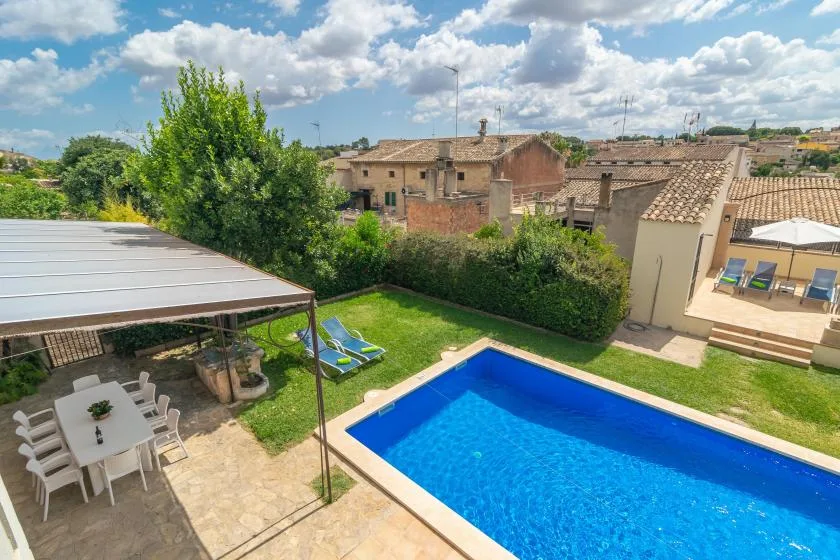 Una piscina y un patio verde junto a una zona de comedor exterior a la sombra.