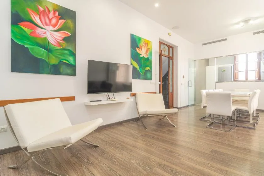 Una luminosa sala de estar y comedor con asientos, un televisor y cuadros florales.