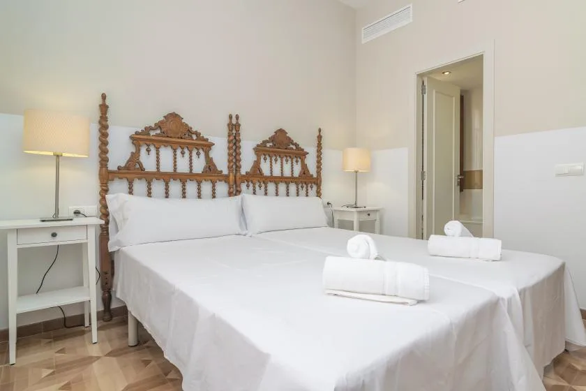 Un dormitorio con una cama bien tendida, ropa de cama blanca y lámparas de noche.