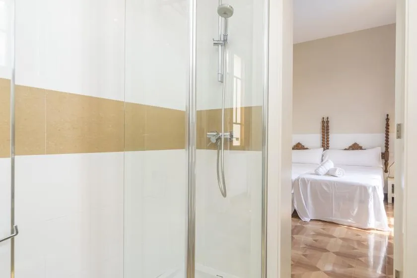 La zona de ducha da a un dormitorio con una cama bien arreglada.