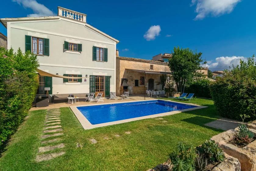 Una piscina azul está en un jardín con césped junto a una casa clara.