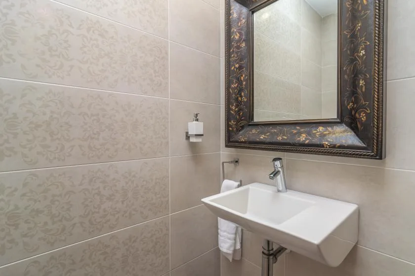 Un lavabo de baño está bajo un espejo grande enmarcado, sobre paredes de azulejos.