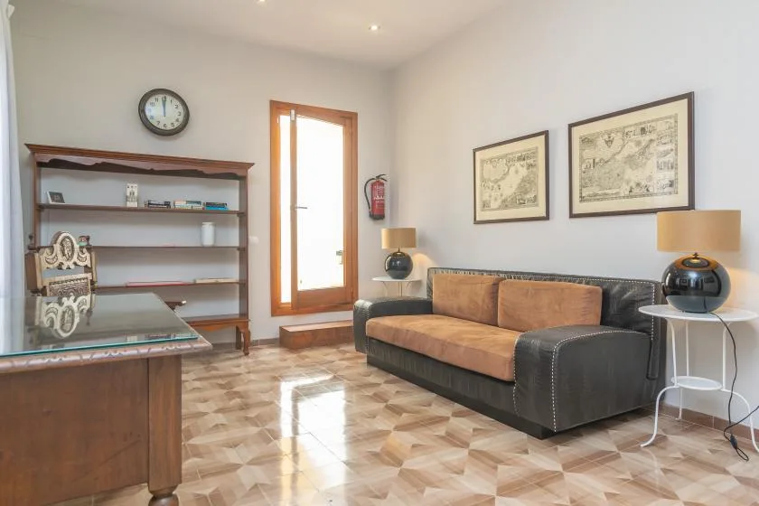 Una sala de estar con un sofá oscuro, un escritorio de madera y cuadros en la pared.