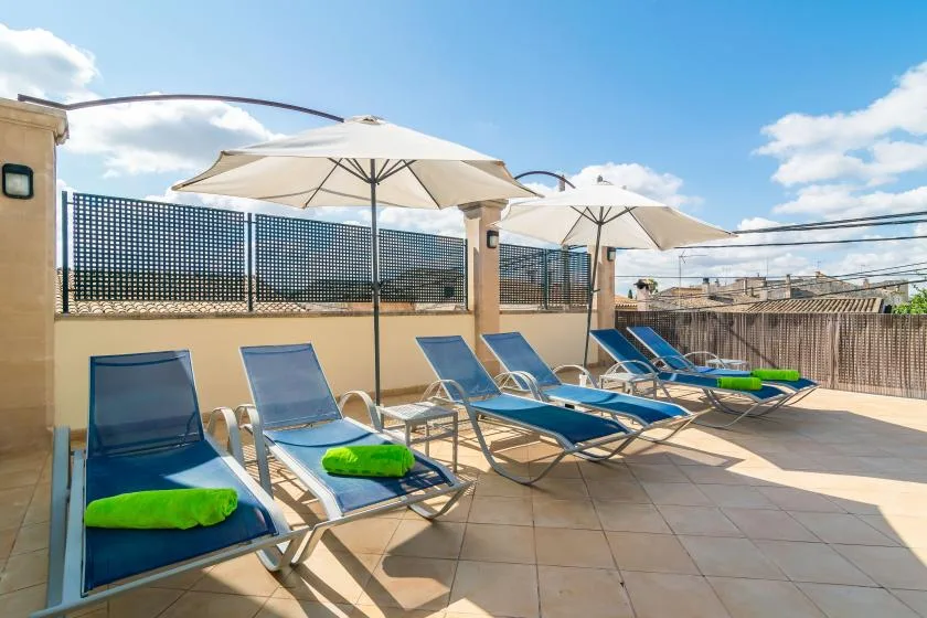 Una terraza soleada en la azotea tiene filas de tumbonas bajo grandes sombrillas.