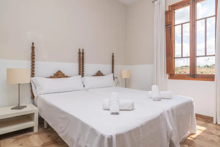 Un dormitorio luminoso con ropa de cama blanca y una gran ventana con marco de madera.