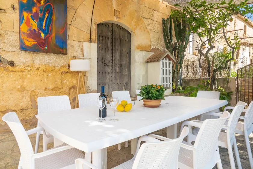 Un comedor al aire libre con una mesa blanca larga y sillas junto a un muro de piedra.