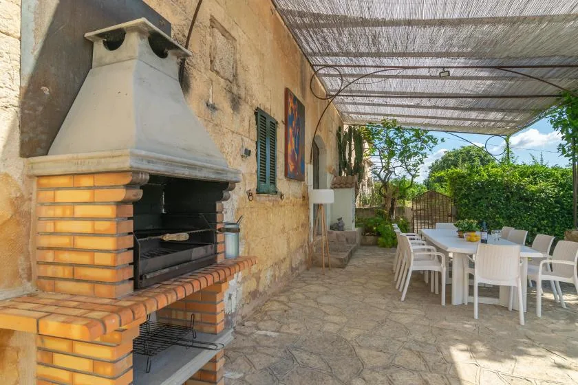 Comedor exterior cubierto con una barbacoa empotrada junto a la mesa.