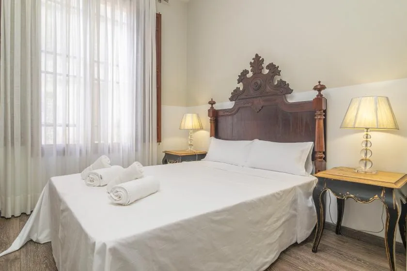 Un dormitorio con una cama blanca, un cabecero de madera tallada y mesas de noche.