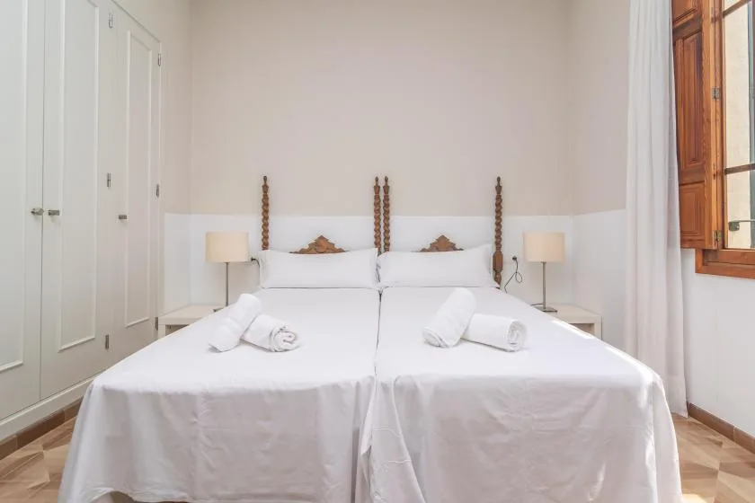 Un dormitorio luminoso con dos camas, lámparas de noche y una ventana.