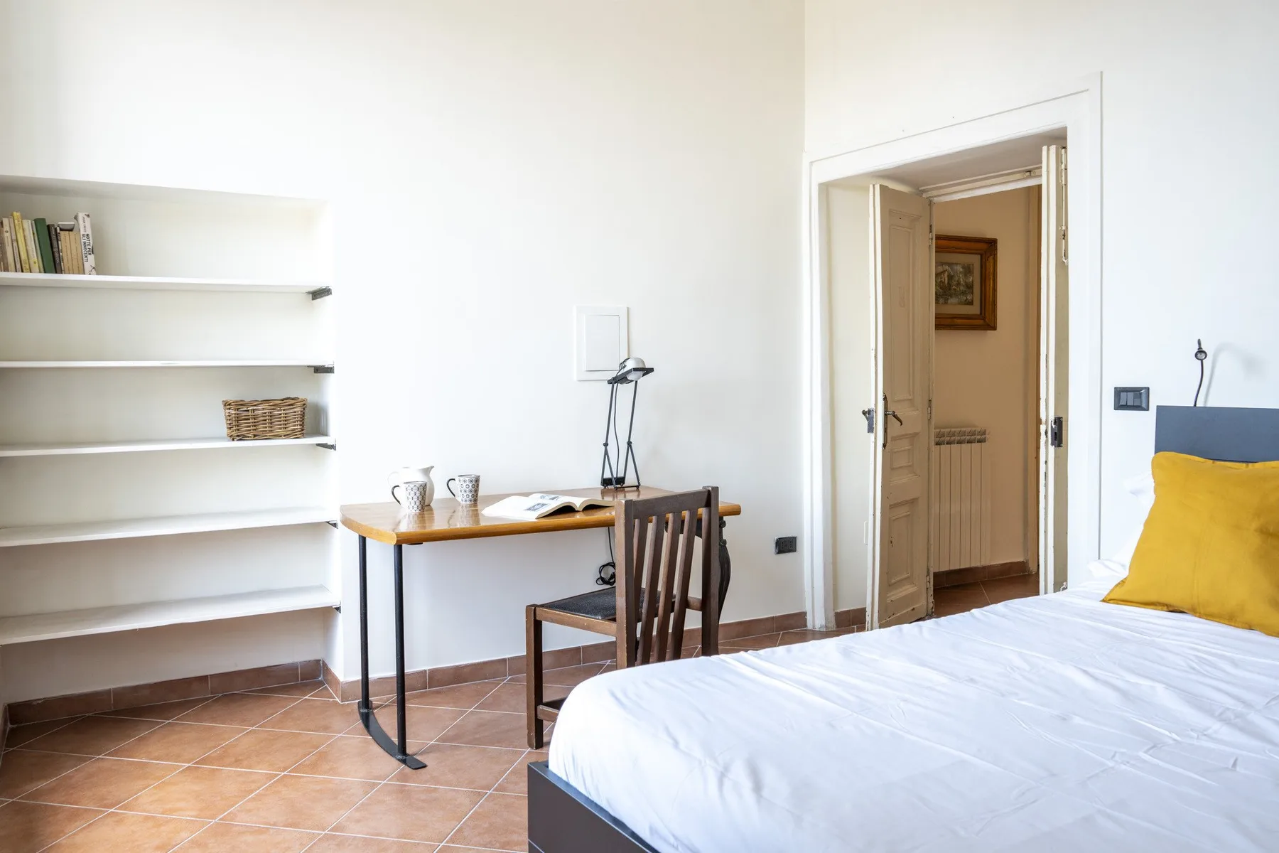 A bedroom with a bed, desk, and open doorway.