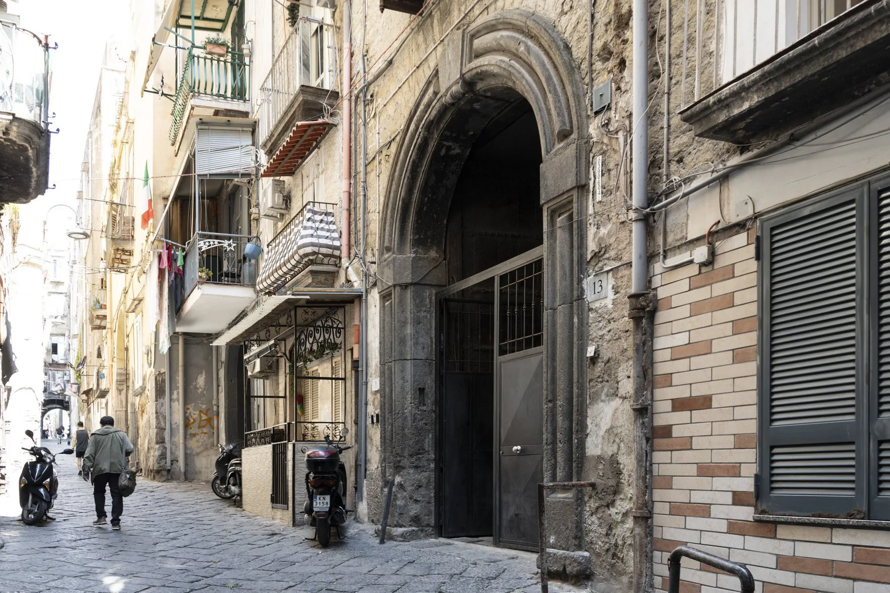 A narrow cobbled street lined with buildings and an arched entrance.