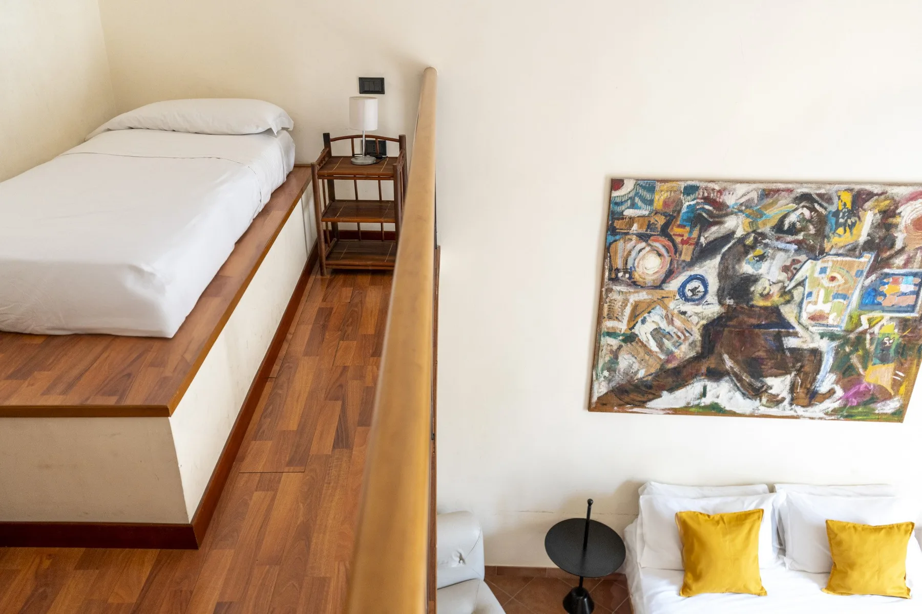 A bedroom with a raised bed beside a lower seating area and colorful wall art.