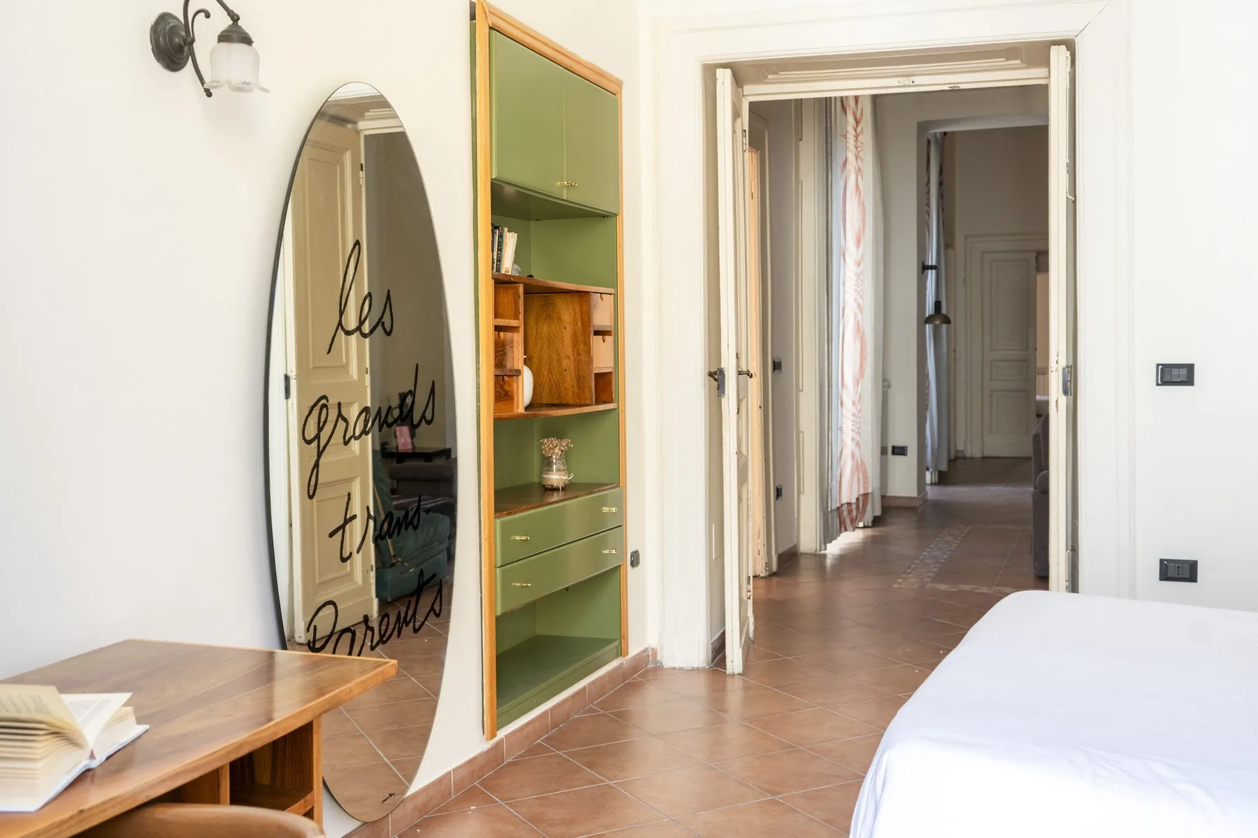 A bright bedroom with a bed beside a doorway leading to a hallway.