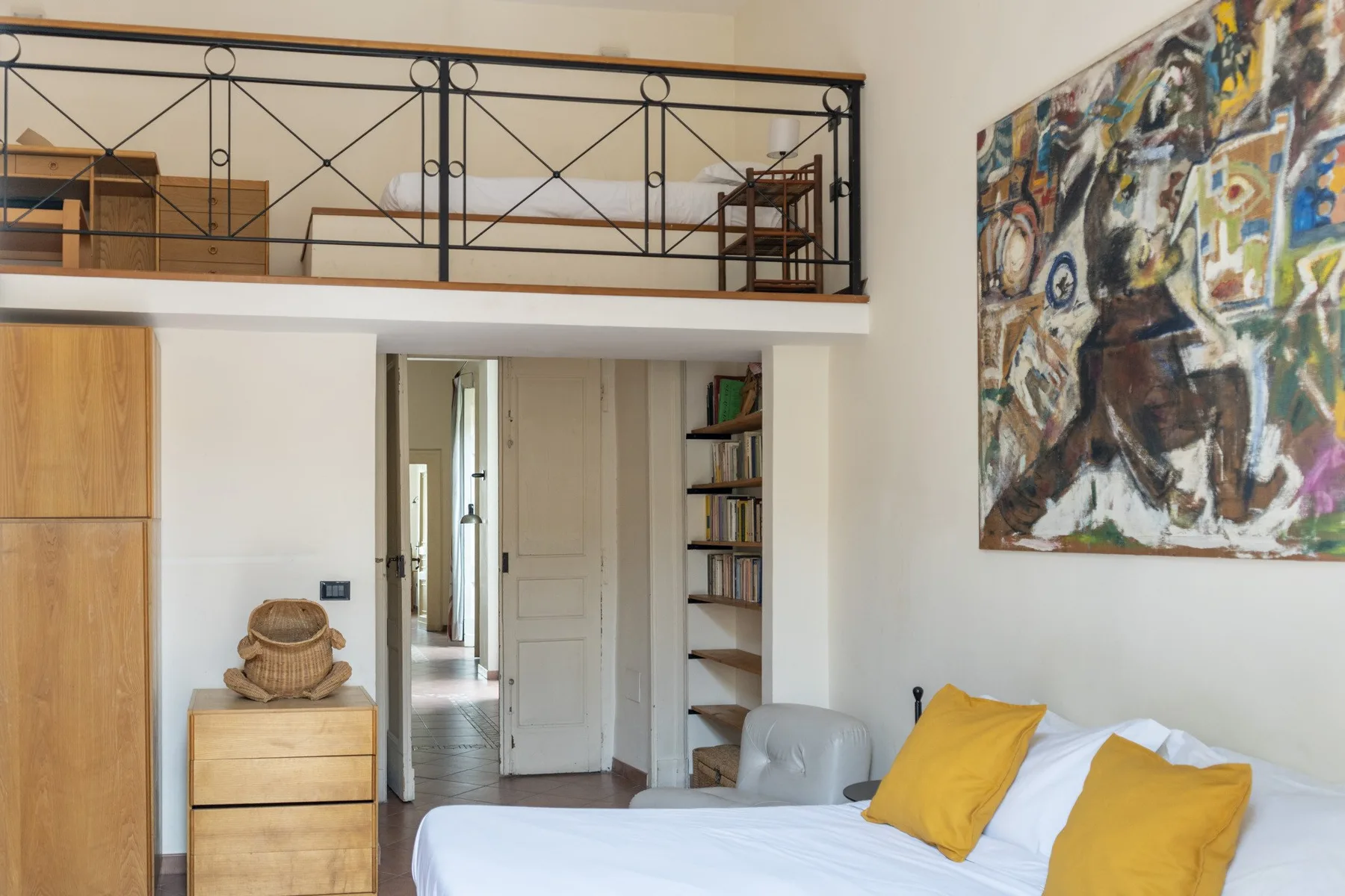 A bedroom with a bed, yellow pillows, and a large painting on the wall.