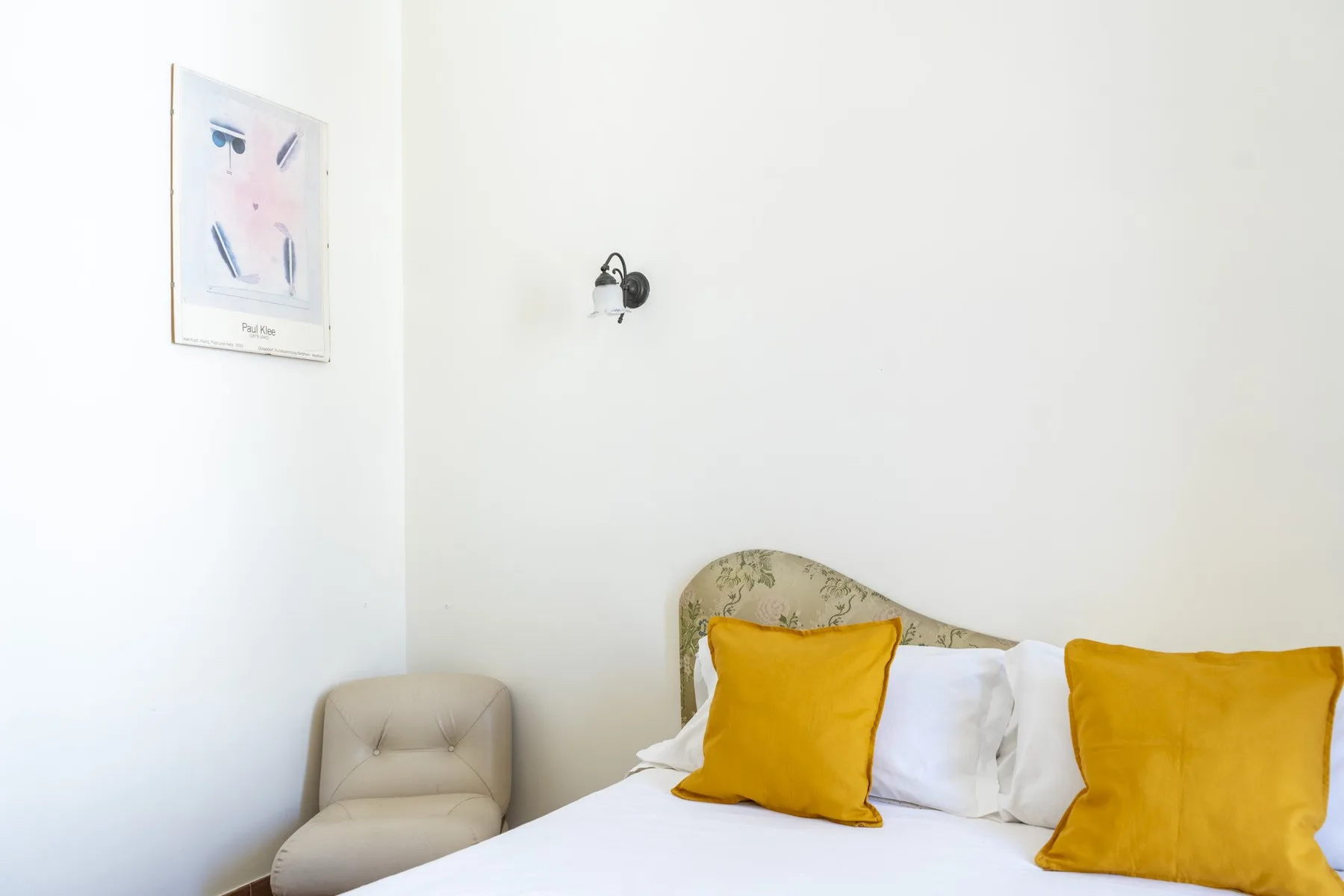 A bedroom with a bed, mustard-colored pillows, and a small upholstered seat.