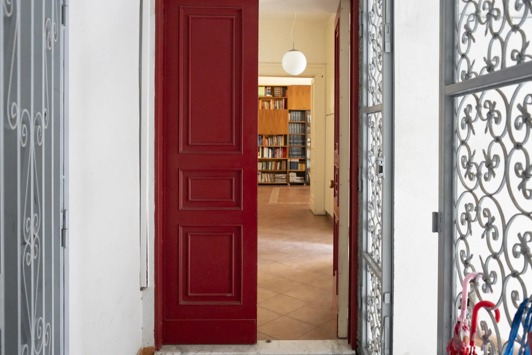 An open red door reveals a tiled hallway with bookshelves at the end.