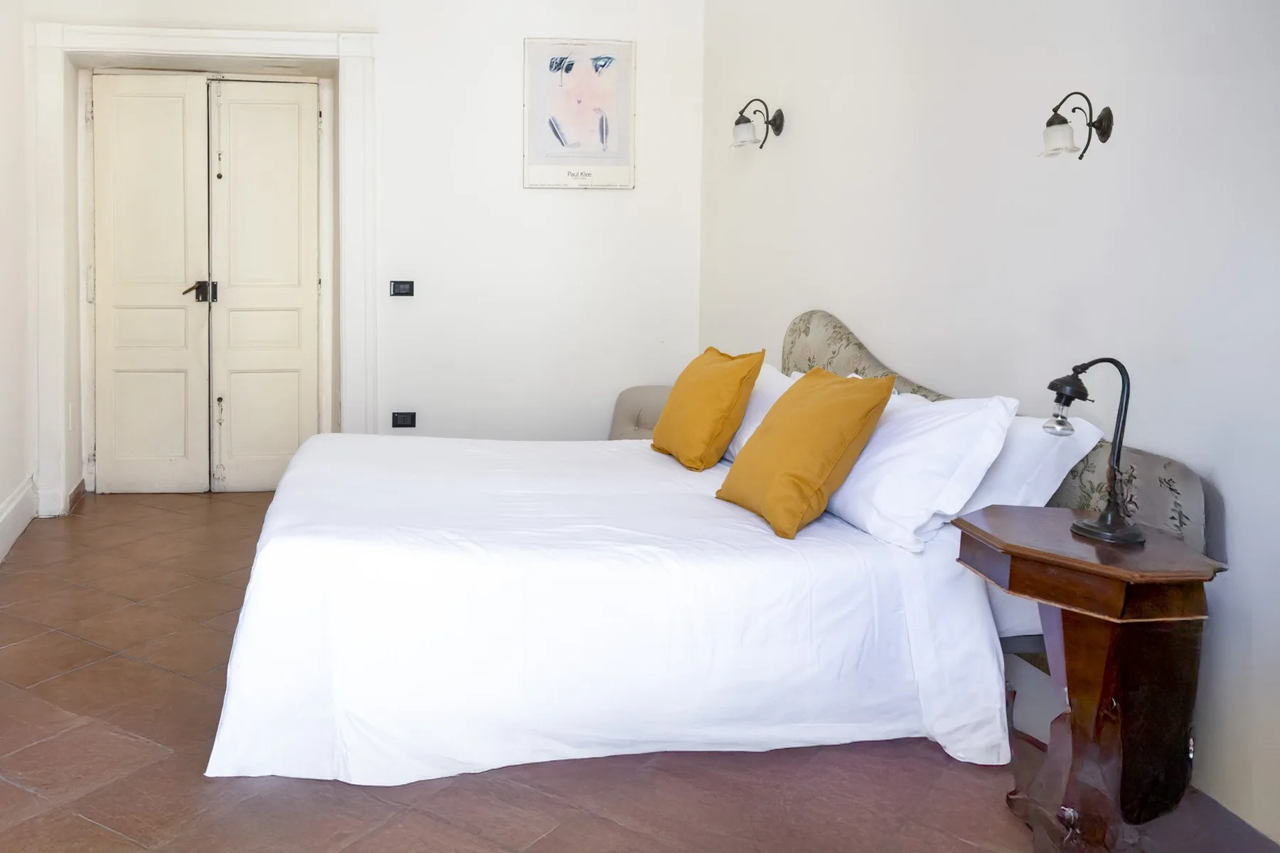 A bedroom with a bed dressed in white and two mustard-colored pillows.