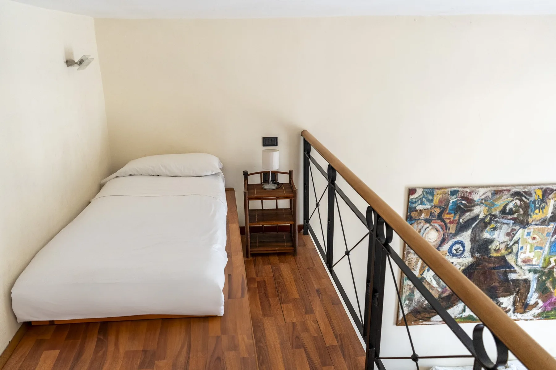 A compact sleeping area with a single bed beside a wooden railing.