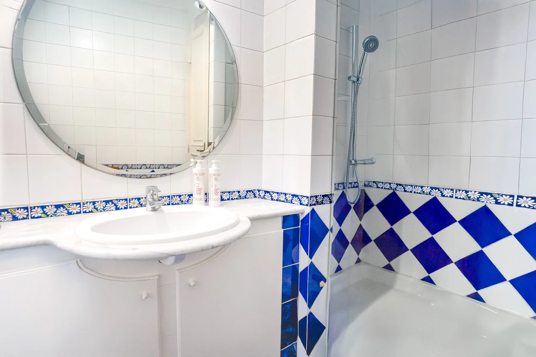 A tiled bathroom with a sink, round mirror, and shower.