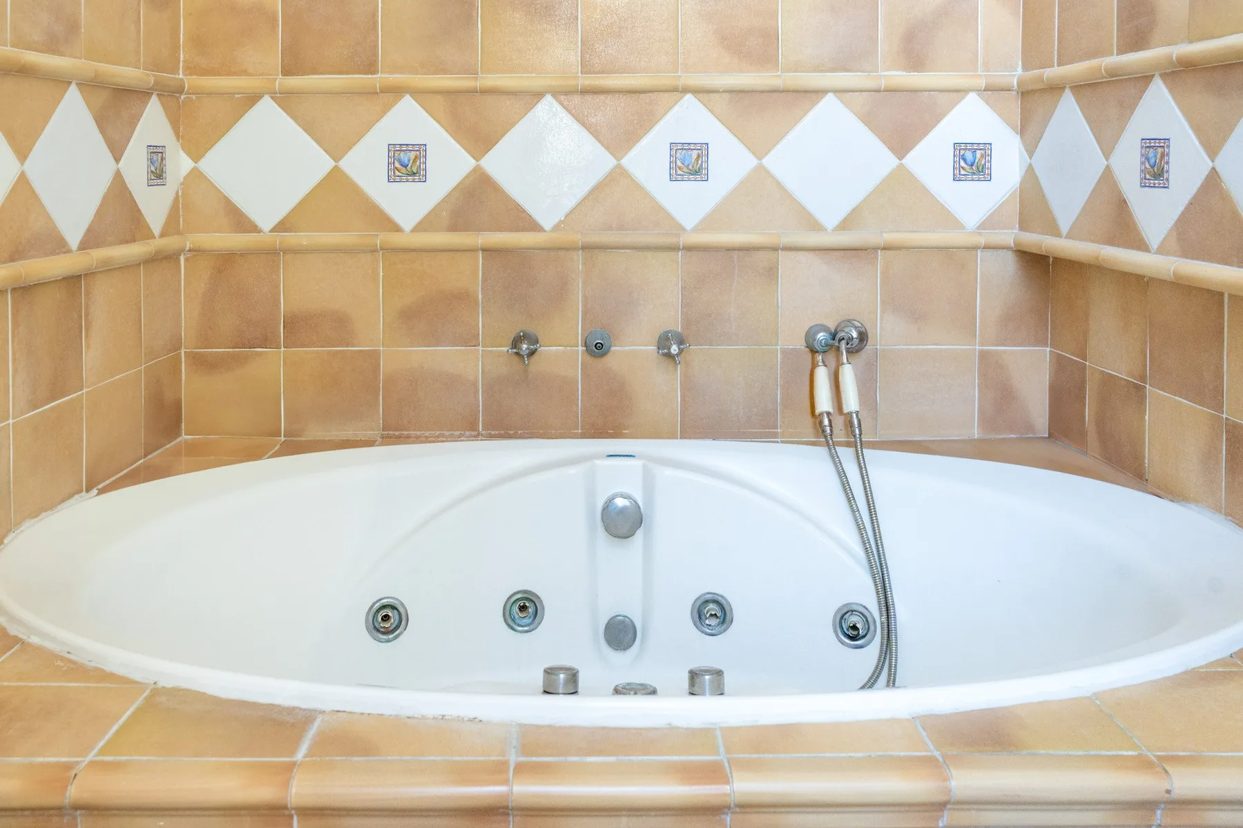 A built-in bathtub sits against a tiled wall, with a handheld shower attachment.