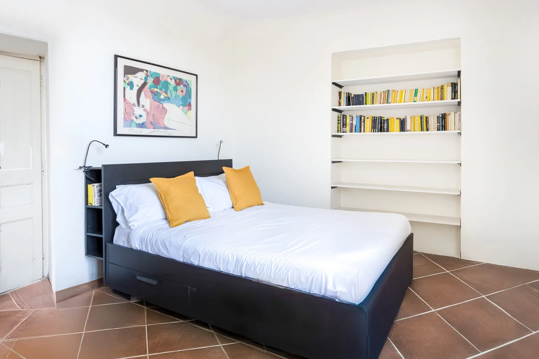 Un dormitorio con una cama, almohadas de colores y una estantería empotrada.