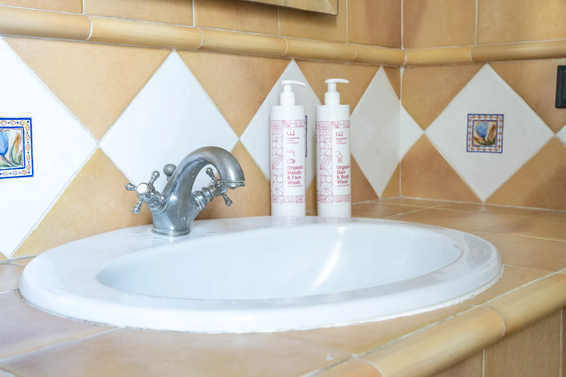 A bathroom sink sits beneath a tiled backsplash, with bottles beside the faucet.