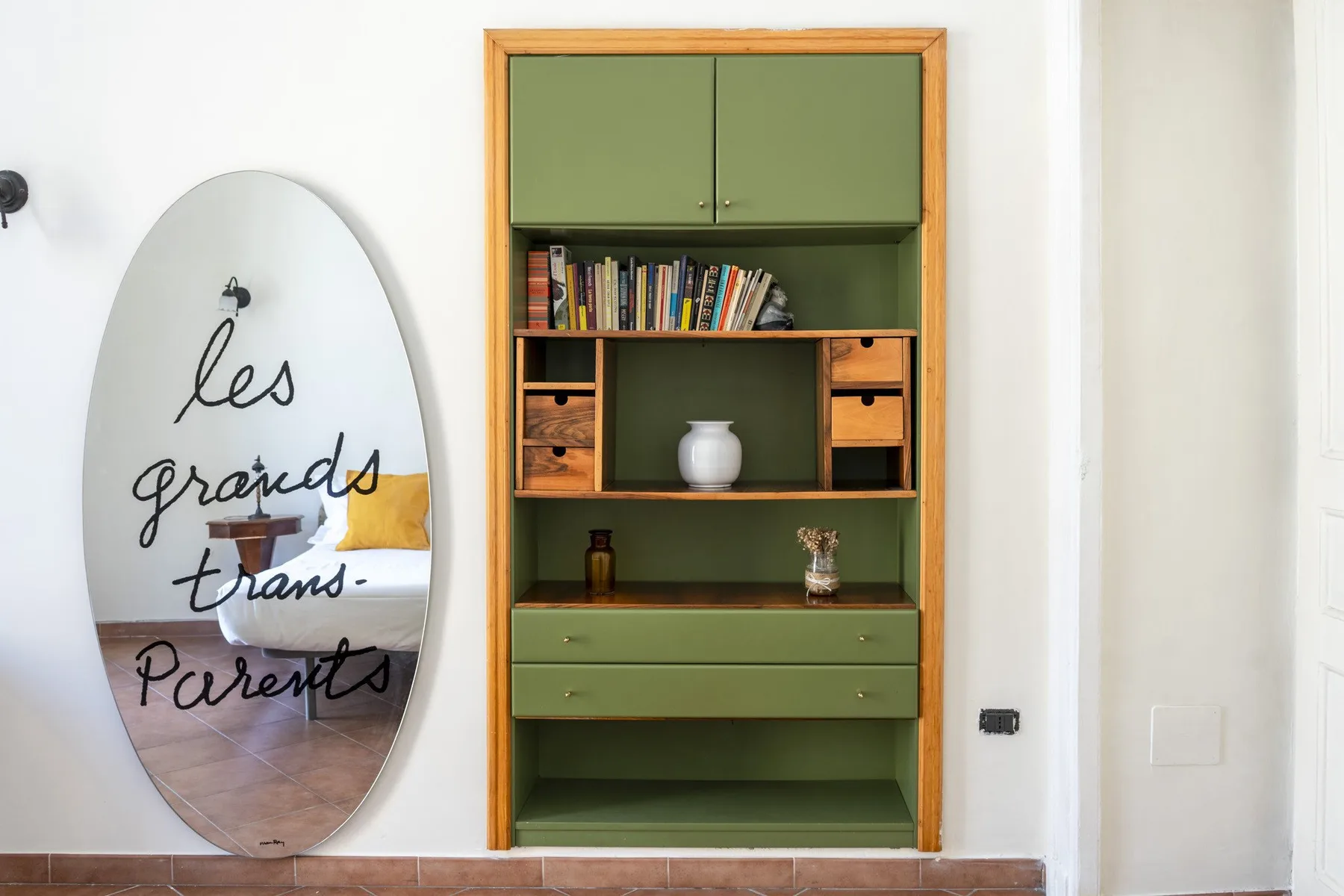 A built-in green bookcase stands beside an oval wall mirror.