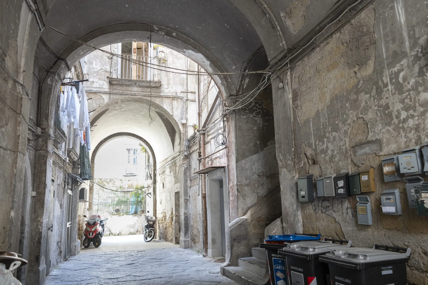 A narrow stone passage with arched ceilings, utility meters, and parked scooters.