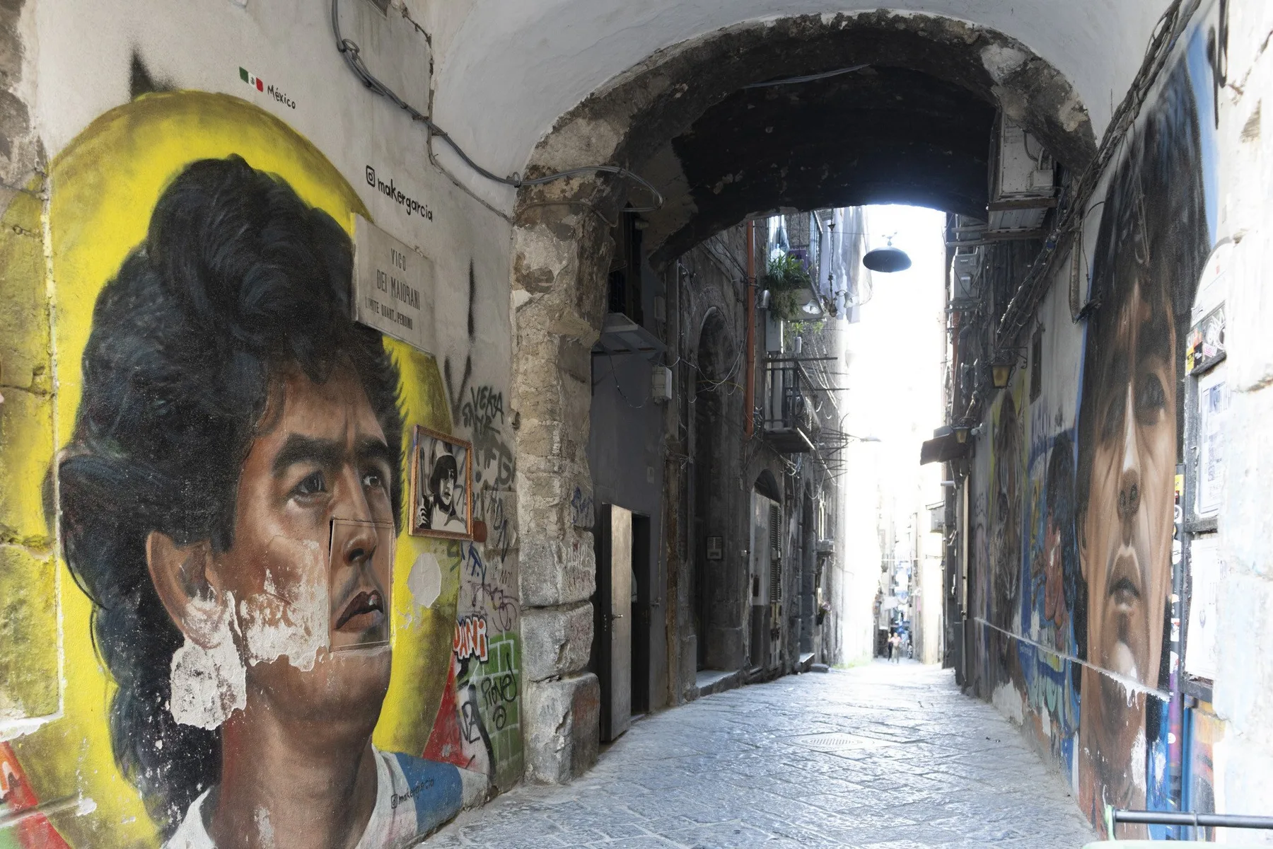 A narrow stone alley is lined with colorful murals and graffiti.