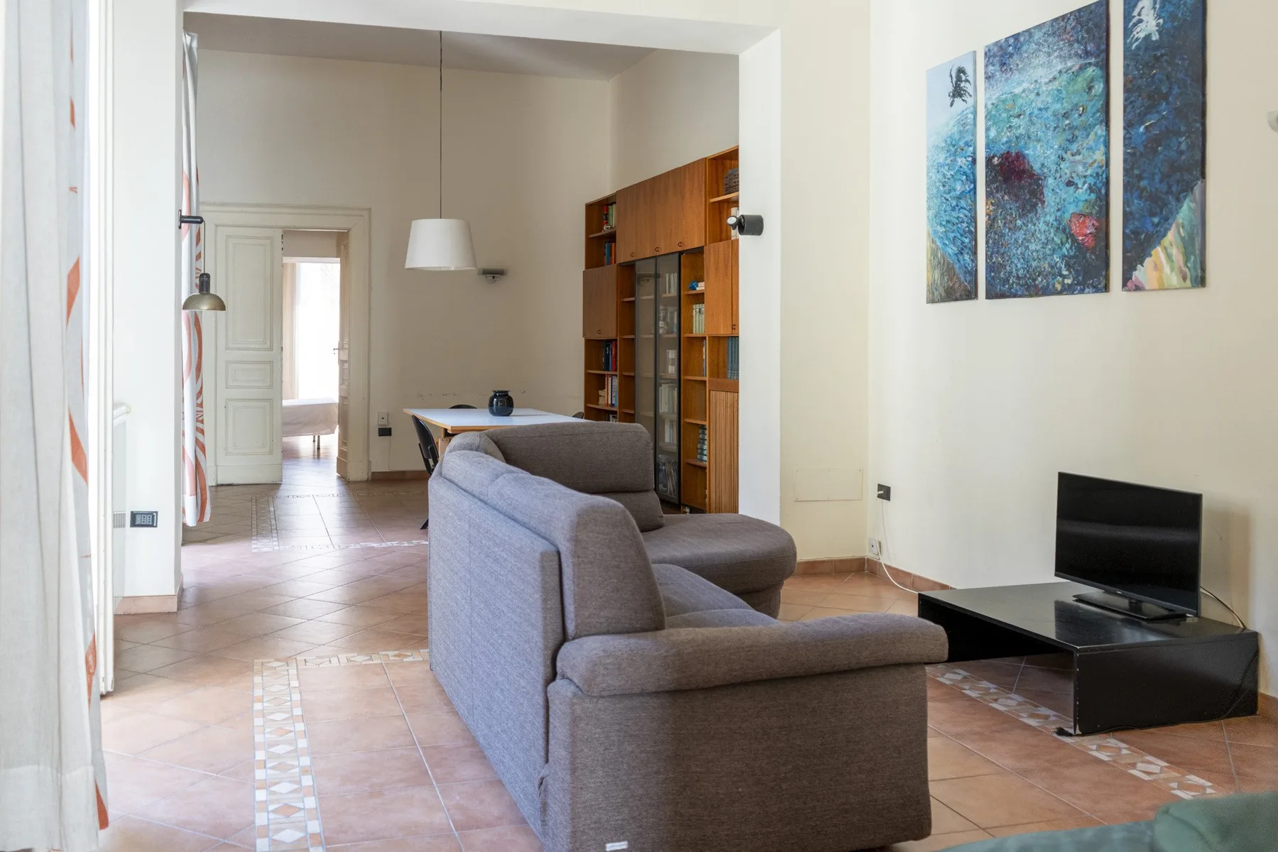 A living room with gray seating, a television, and a tall wooden bookcase.